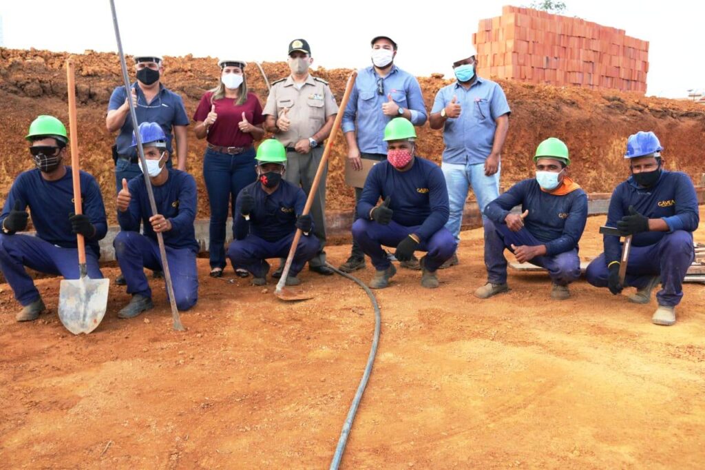 Funcionários com capacete e máscaras seguram a enxada