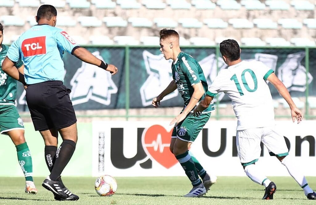 Lance do jogador da Caldense (verde) com a bola sendo marcado pelo atleta do Gama (branco)